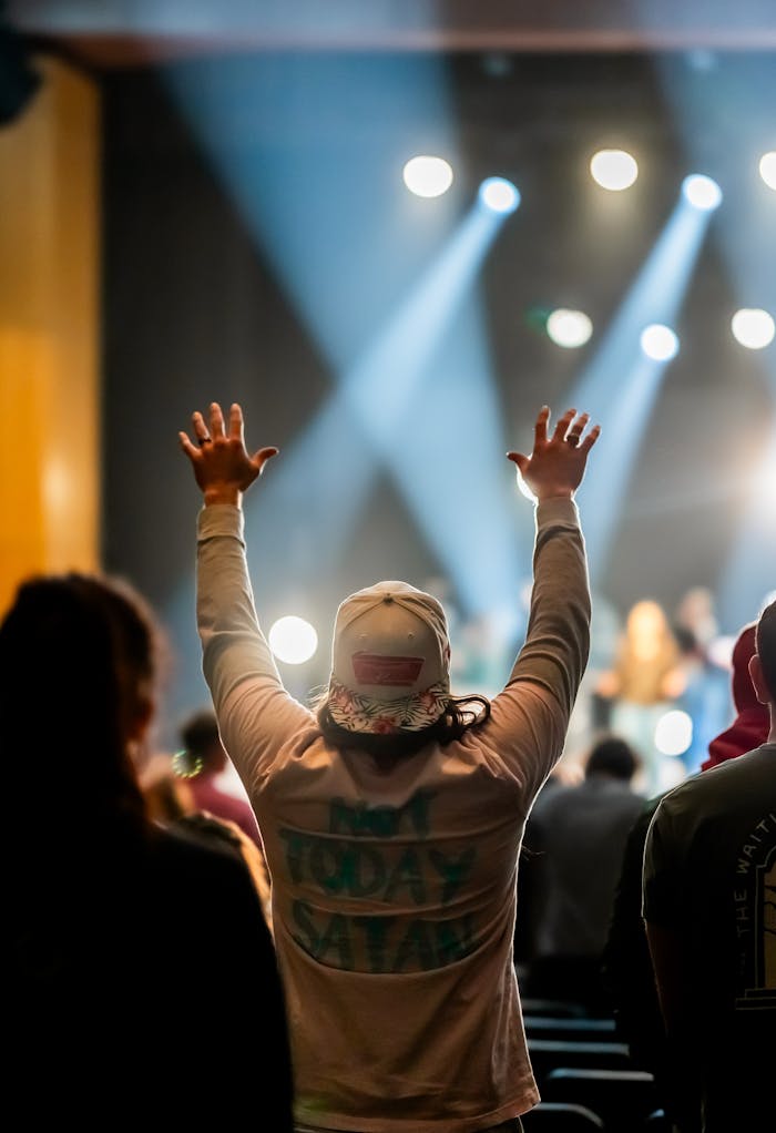 Crafting Captivating Headlines: Your awesome post title goes here A crowd with raised hands during a lively indoor worship concert with stage lights.